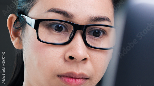 Close-up eyes of Asian woman with glasses working on a laptop computer in her office.