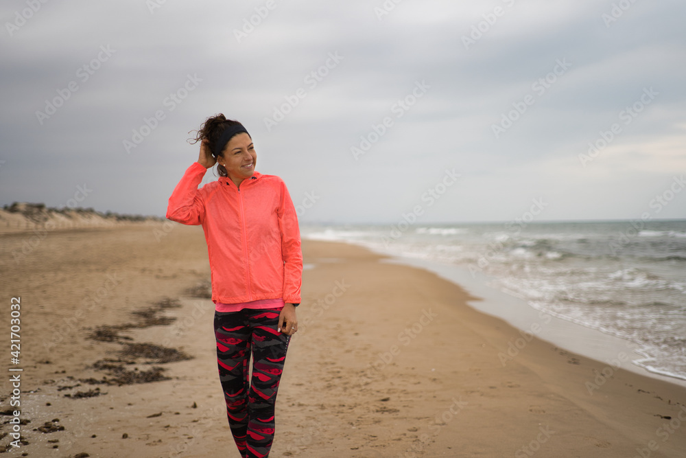 Happy young woman wearing sports clothes smiling after workout in the beach.