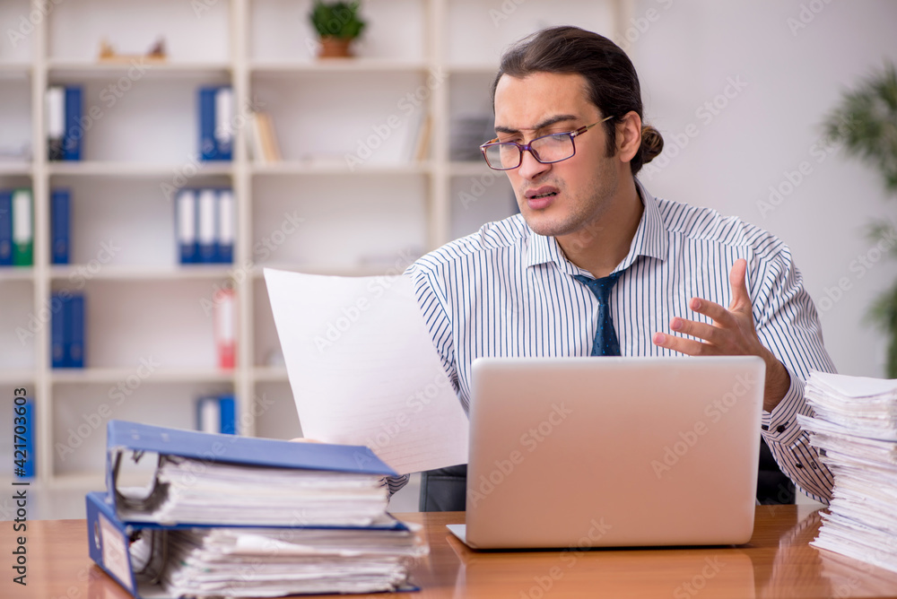 Young male employee unhappy with excessive work in the office Young male employee unhappy with excessive work in the office