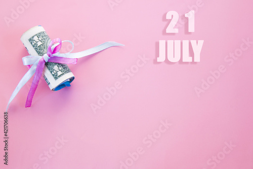 calendar date on pink background with rolled up dollar bills pinned by pink and blue ribbon with copy space. July 21 is the twenty first day of the month