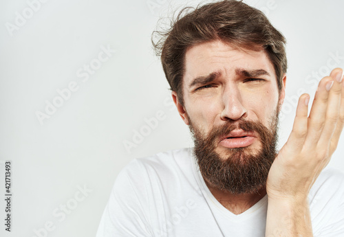 A man gestures with his hands on a light background in a white t-shirt cropped view