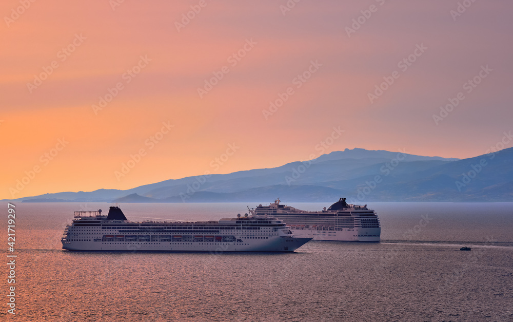 Two big tourist cruise liners manoeuvre in harbor. Beautiful sunset sky and distant hazy islands. Sea voyage, comfort, adventure, romantic honeymoon.