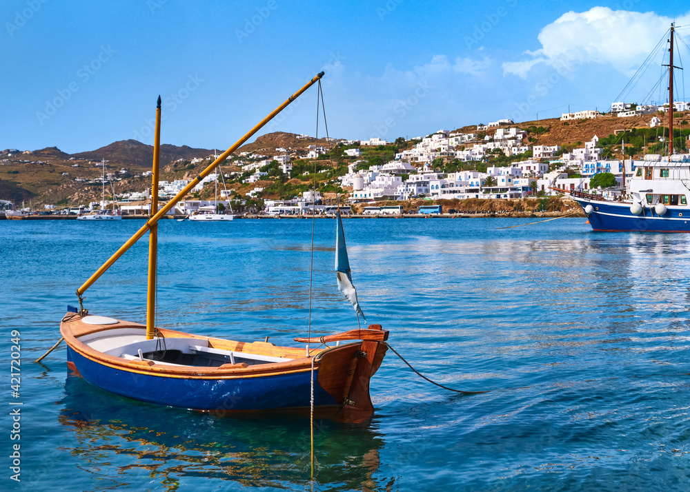 Beautiful summer day in typical Greek island. Fishing boats, whitewashed house. Small blue boat in foreground. Mykonos, Cyclades, Greece.