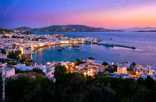 Colorful view after sunset over town of Mykonos, Cyclades, Greece, harbor and port, cruises, ship, whitewashed houses. Colorful town lights up.