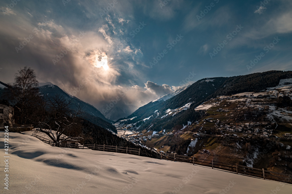 Clouds, snow mountains and Tyrolean village in the foreground.2021