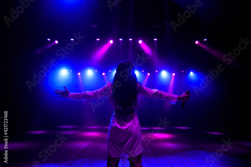 Unrecognizable singer standing on stage at microphone, back view, neon lights