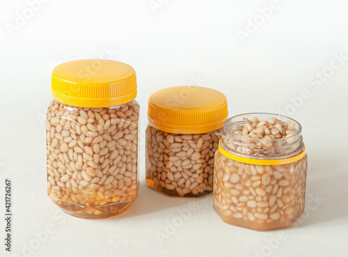 Pine nut with honey In a transparent jar with a yellow lid. Nearby are jars of nuts and honey. Place for a label. Close-up. Light background.