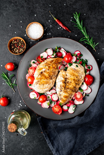 Grilled chicken breast and salad with fresh vegetables, tomatoes and radishes in a plate Chicken meat with salad. Healthy food on stone background