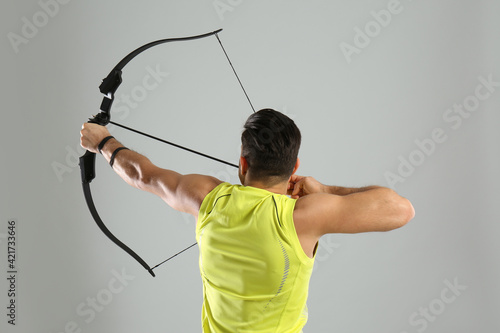 Man with bow and arrow practicing archery on light grey background, back view