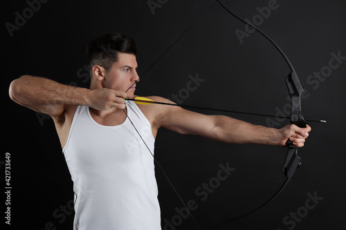 Man with bow and arrow practicing archery on black background