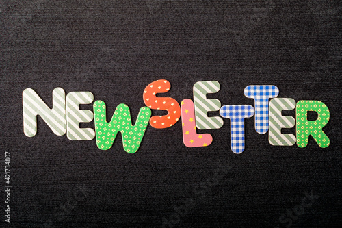 Wallpaper Mural Card with Newletter word made from mixed vivid colored wooden letters on a textured dark black textile material that can be used as a message. Torontodigital.ca