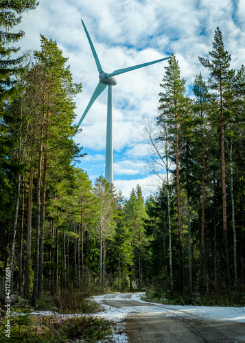 Wind turbine natuarally framed by trees with a snow covred road leading to it. At hjo, sweden