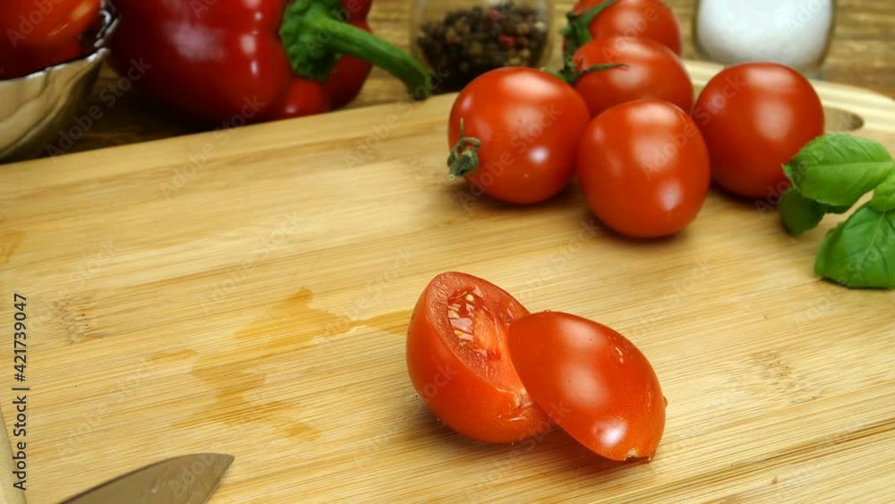 Chef hands cut cherry tomato into pieces with sharp kitchen knife on wooden cutting board for preparing delicious food. Home kitchen. Close-up. Chef hands cut cherry tomato into pieces with sharp kitchen knife on wooden cutting board for preparing delicious food. Home kitchen. Close-up.