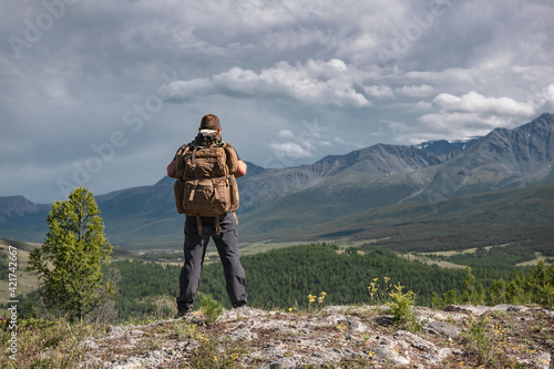 Hiker stands with backpack on background of mountains