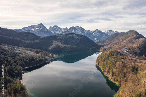 Aerial drone shot of Alpsee lake in Fussen with view of Alps snow mountain range in Germany winter