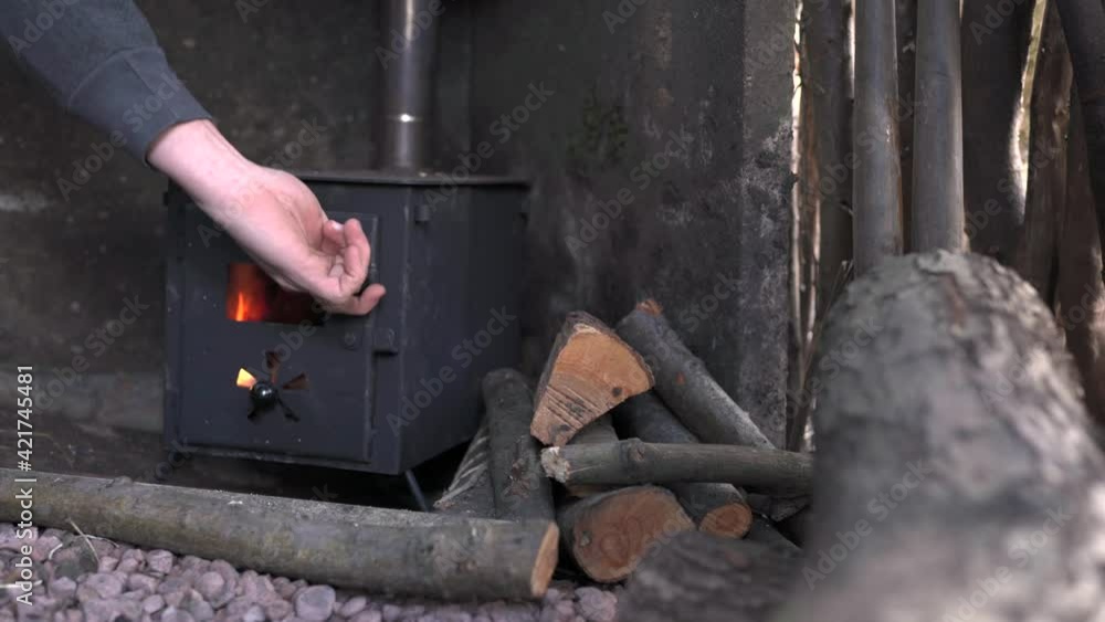 The hands of a person putting a wooden log into a wood burning camp stove The hands of a person putting a wooden log into a wood burning camp stove