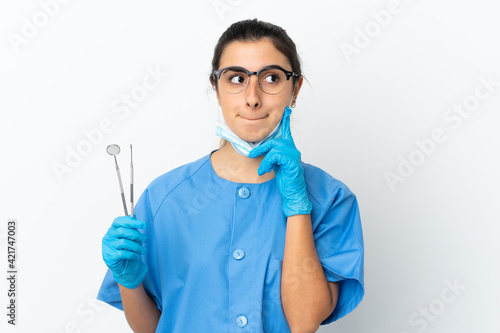 Young woman dentist holding tools isolated on white background having doubts and thinking