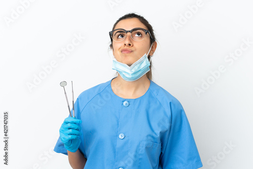 Young woman dentist holding tools isolated on white background and looking up