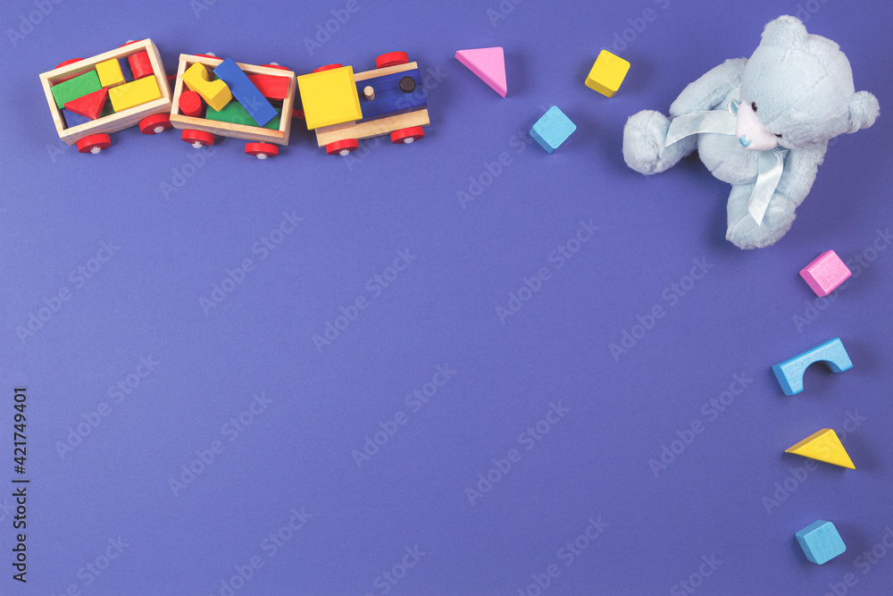 Obraz premium Baby kids toys background. Wooden train, blue teddy bear and colorful blocks on navy blue background