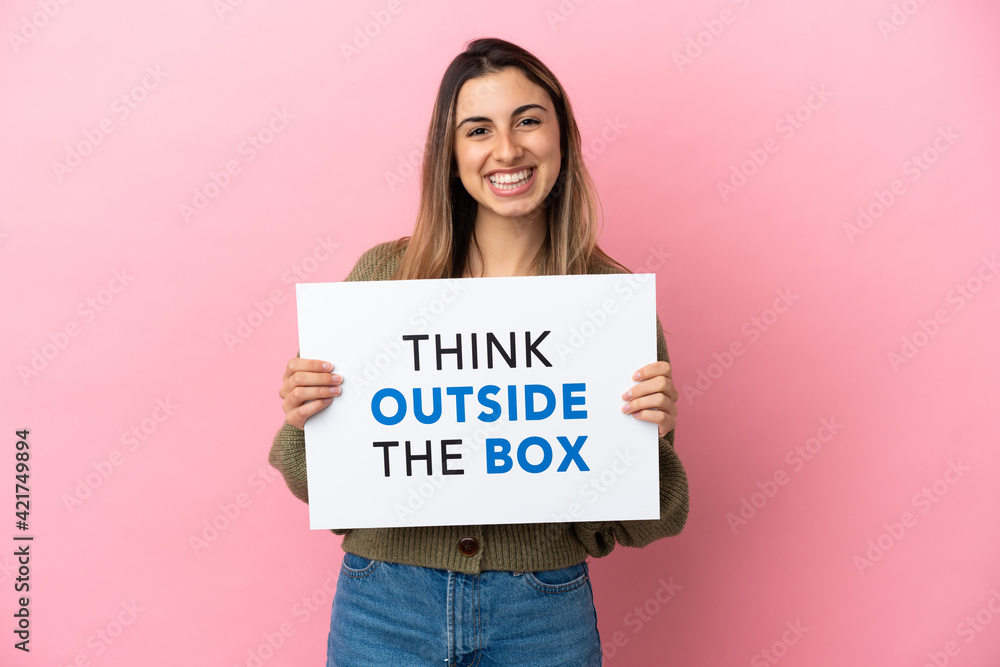Young caucasian woman isolated on pink background holding a placard with text Think Outside The Box Young caucasian woman isolated on pink background holding a placard with text Think Outside The Box