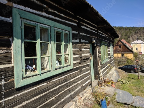 Old wooden traditional cabin with green window frames located in the village welcoming the spring season during sunny day