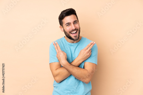 Caucasian handsome man isolated on beige background smiling and showing victory sign