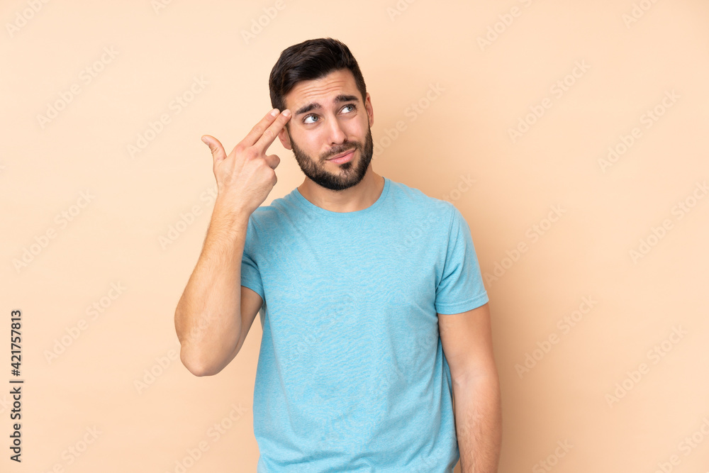 Caucasian handsome man isolated on beige background with problems making suicide gesture Caucasian handsome man isolated on beige background with problems making suicide gesture