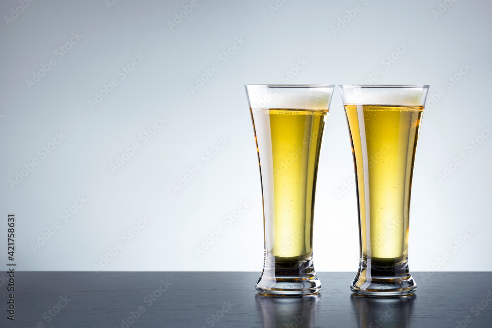Two glass of beer on dark wooden table against grey background with copy space. Two glass of beer on dark wooden table against grey background with copy space.