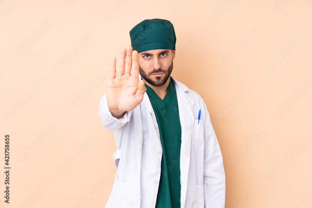 Surgeon man isolated on beige background making stop gesture with her hand Surgeon man isolated on beige background making stop gesture with her hand