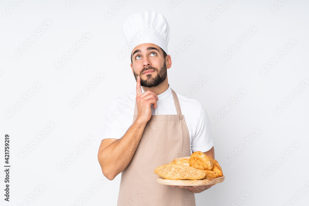 Male baker holding a table with several breads isolated on white background thinking an idea Male baker holding a table with several breads isolated on white background thinking an idea