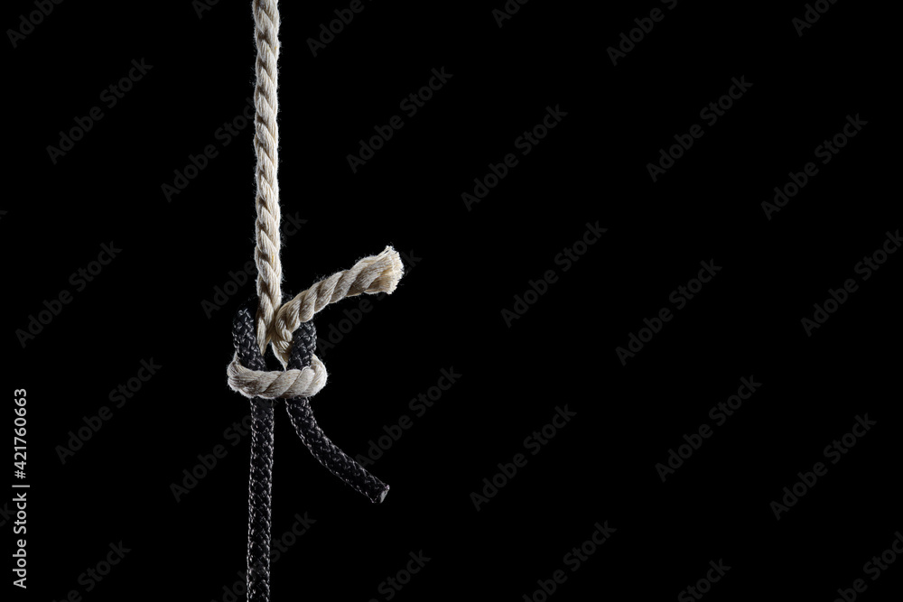 Black and white ropes are tied in a knot on a black background