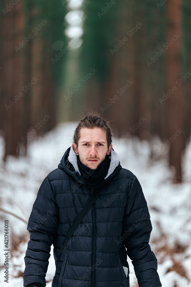 Handsome young man standing in a snowy forest looking straight into the camera Handsome young man standing in a snowy forest looking straight into the camera
