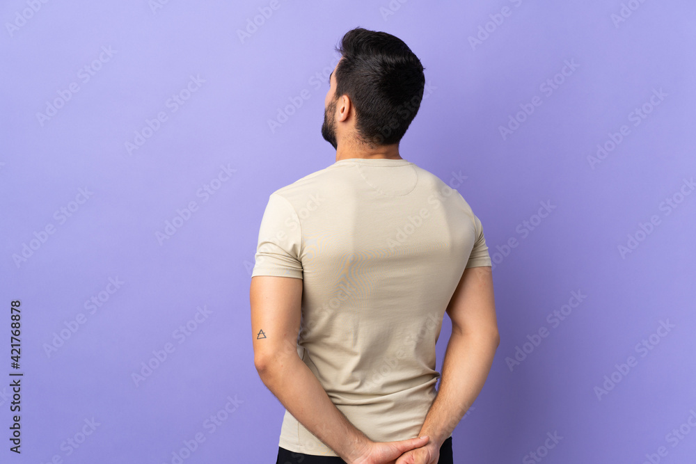 Young handsome man with beard over isolated background in back position and looking back Young handsome man with beard over isolated background in back position and looking back