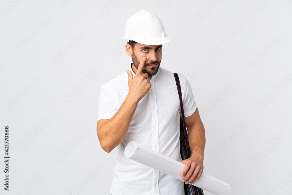 Young architect man with helmet and holding blueprints isolated on white background showing something