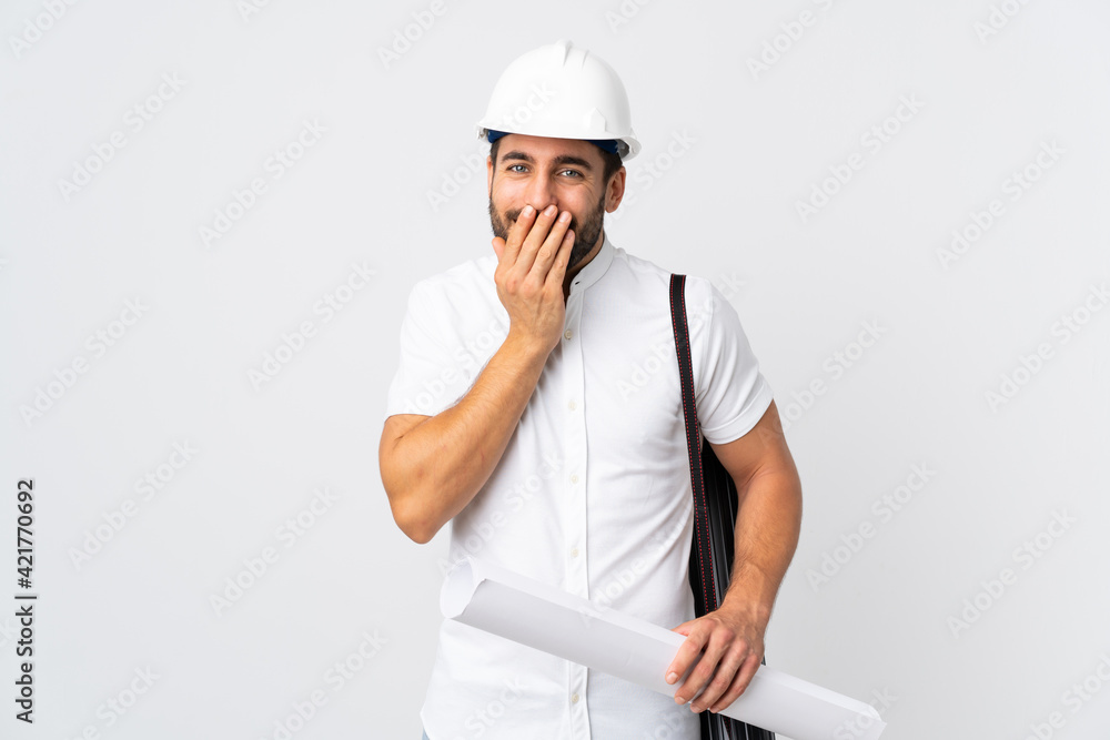 Young architect man with helmet and holding blueprints isolated on white background happy and smiling covering mouth with hands Young architect man with helmet and holding blueprints isolated on white background happy and smiling covering mouth with hands
