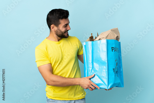 Young caucasian man holding a recycle bag isolated on blue background with happy expression