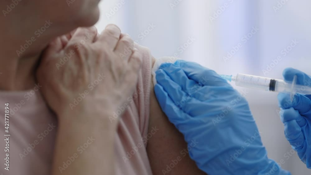 Mass vaccination. Close up view of medical worker in protective gloves disinfecting skin before giving vaccine shot in arm of pensioner person. Concept of vaccination, infectious disease prevention. Mass vaccination. Close up view of medical worker in protective gloves disinfecting skin before giving vaccine shot in arm of pensioner person. Concept of vaccination, infectious disease prevention.
