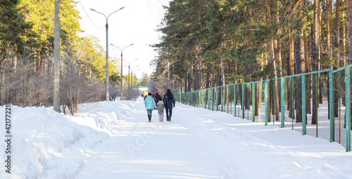 People walk along a wide forest road. Walk in the winter park. Beautiful bright winter landscape. Copy space.