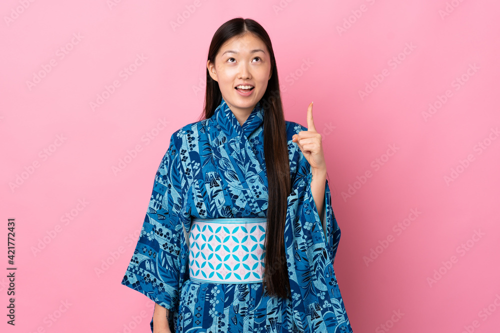 Young Chinese girl wearing kimono over isolated background pointing up and surprised Young Chinese girl wearing kimono over isolated background pointing up and surprised