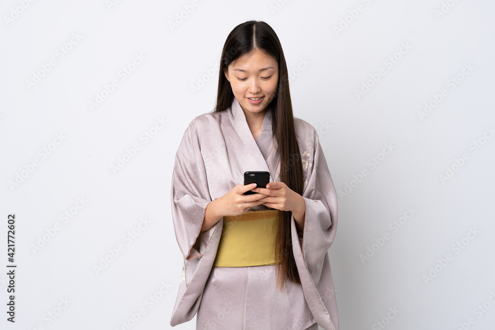 Young Chinese girl wearing kimono over isolated background sending a message with the mobile Young Chinese girl wearing kimono over isolated background sending a message with the mobile