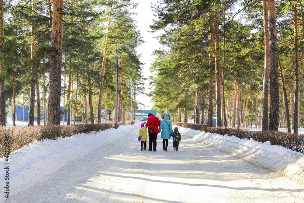 A family with children walks in a winter park on a sunny day. Bright winter landscape. Family joint outdoor recreation. Copy space. A family with children walks in a winter park on a sunny day. Bright winter landscape. Family joint outdoor recreation. Copy space.