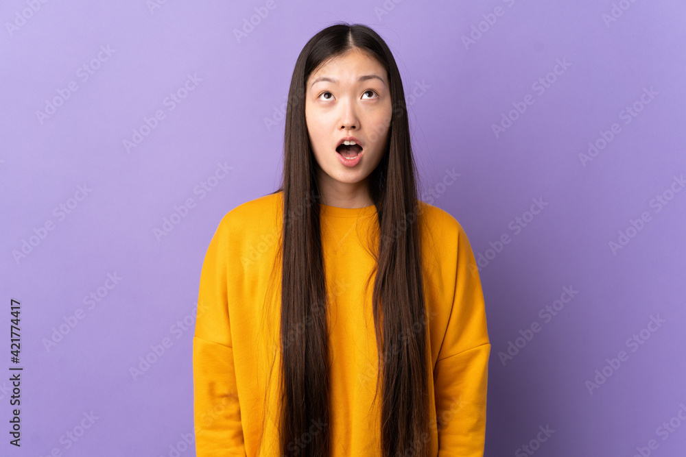 Young Chinese girl over isolated purple background looking up and with surprised expression Young Chinese girl over isolated purple background looking up and with surprised expression