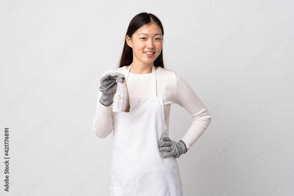 Chinese fishmonger wearing an apron and holding a raw fish over isolated white background posing with arms at hip and smiling Chinese fishmonger wearing an apron and holding a raw fish over isolated white background posing with arms at hip and smiling