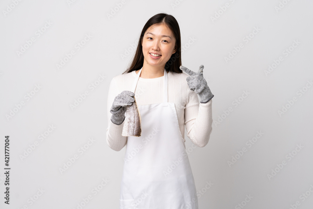 Chinese fishmonger wearing an apron and holding a raw fish over isolated white background giving a thumbs up gesture Chinese fishmonger wearing an apron and holding a raw fish over isolated white background giving a thumbs up gesture