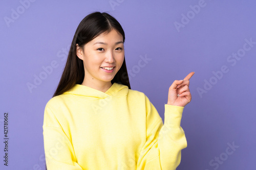 Young asian woman isolated on purple background pointing finger to the side © luismolinero