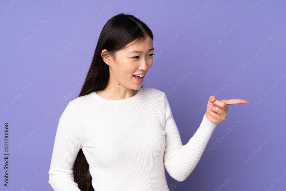 Young asian woman isolated on purple background pointing finger to the side and presenting a product Young asian woman isolated on purple background pointing finger to the side and presenting a product