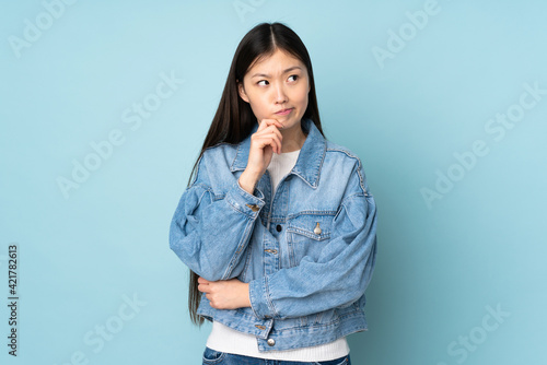Fotografie Young asian woman isolated on background having doubts and thinking