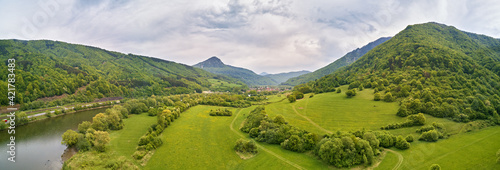 Village, river and road in mountain valley. Green mountain meadows and hills. Kraľoviansky meander on river Bar. Spring panorama