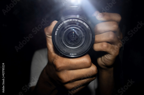 A reflection in a mirror of a man with camera in hand looking through the camera lens.