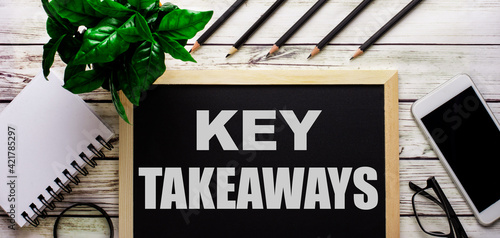 KEY TAKEAWAYS is written in white on a black board next to a phone, notepad, glasses, pencils and a green plant. photo